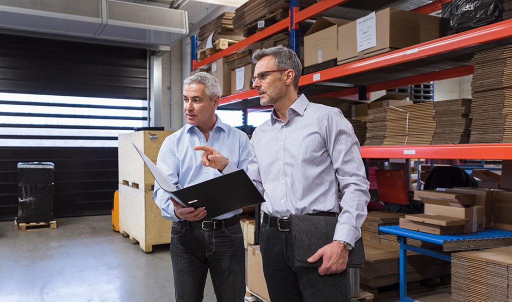 Two male professionals having a meeting in a warehouse and looking at products