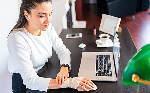 An employee working in an office, looking at her bandaged arm at her desk.